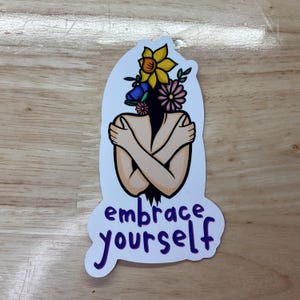 May include: A white sticker with a colorful illustration of a person hugging themself with flowers growing from their head. The text "embrace yourself" is written in purple below the illustration.