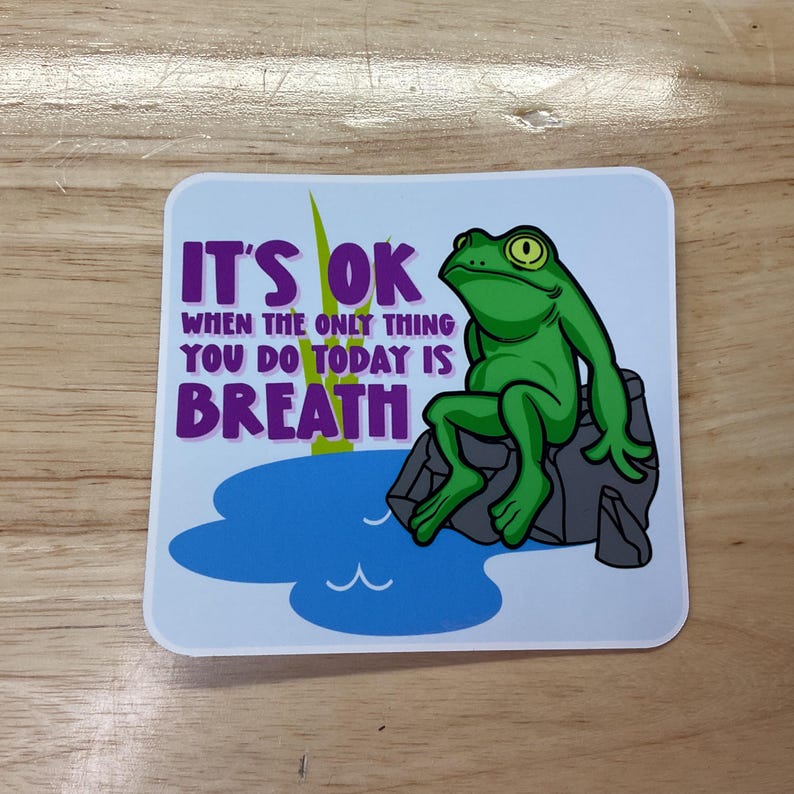May include: A sticker with a green frog sitting on a rock in a pond. The sticker says "It's OK when the only thing you do today is breathe."