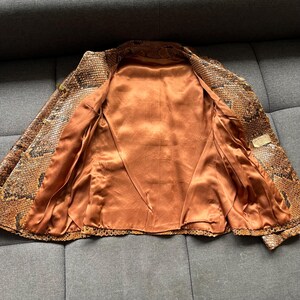 May include: Open view of a snakeskin-patterned jacket. The jacket features a brown and black pattern on the exterior and a copper-colored satin lining. The jacket is unbuttoned, revealing the interior lining. The jacket is a vintage piece.