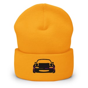 May include: A yellow knitted beanie with a black embroidered silhouette of a car on the front.