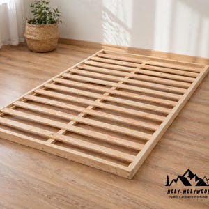 Könnte beinhalten: Ein Bettrahmen aus Naturholz mit Lamellendesign. Der Rahmen ist rechteckig und scheint aus hellfarbigem Holz gefertigt zu sein. Das Logo der Holy-Molywood Family Carpentry Workshop befindet sich unten rechts.