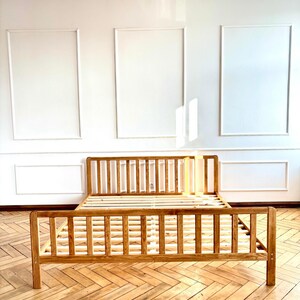 May include: A wooden bed frame with a slatted headboard and footboard, featuring a natural light brown finish and visible wood grain. The structure includes a slatted base for mattress support, with a logo in the top left corner reading HOLY-MOLYWOOD.