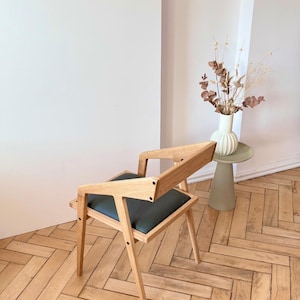 Op de afbeelding: Houten stoel met een donkergrijze zitting en een uniek geometrisch ontwerp. De stoel is gemaakt van lichtgekleurd hout en heeft een moderne uitstraling. De tekst "HOLY-MOLYWOOD Family Carpentry Workshop" is zichtbaar.