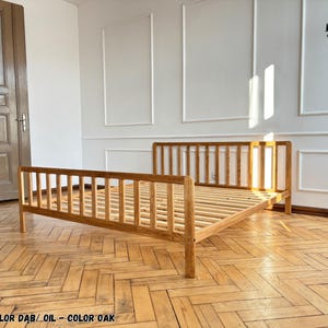 May include: A light brown oak bed frame with a slatted headboard and footboard. The wooden bed features a natural oil finish and a slatted base for mattress support. The frame is constructed with vertical wooden slats on all sides.