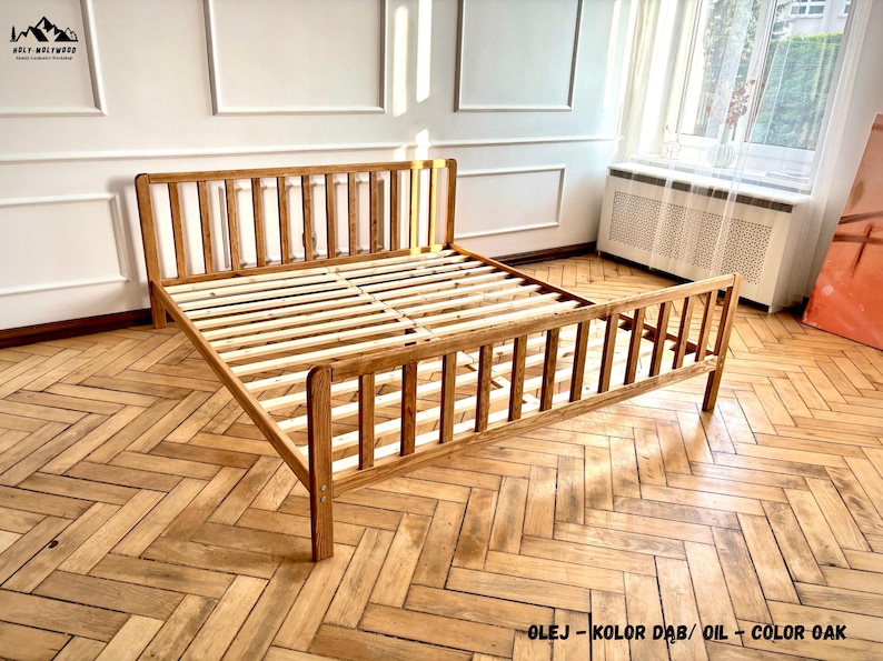 May include: A wooden bed frame with a tall headboard and a lower footboard, both featuring vertical slats. The frame is finished in an oak-colored oil and includes a slatted base for mattress support. The text OLEJ - KOLOR DĄB / OIL - COLOR OAK is visible.