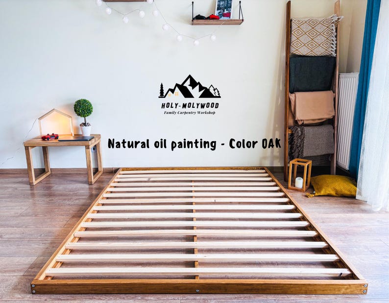 Op de afbeelding: Een houten bedframe met een lattenontwerp, gebeitst in een natuurlijke eikenkleur. Het frame is rechthoekig en staat op een lichtgekleurde vloer. De tekst "Natural oil painting - Color OAK" is zichtbaar.