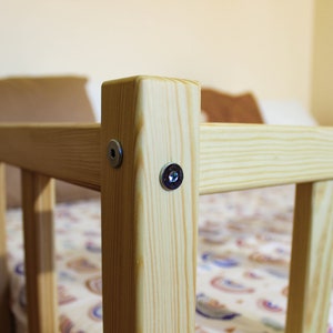 May include: Close-up of a wooden bed frame with two silver screws securing the frame. The bed frame is made of natural wood with a light brown finish.
