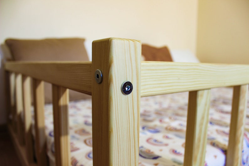 May include: Close-up of a wooden bed frame with two silver screws securing the frame. The bed frame is made of natural wood with a light brown finish.
