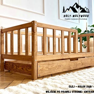 Könnte beinhalten: Ein hell eichenfarbener Bettrahmen aus Holz mit einer Schublade. Das Bett hat ein Lattenrost an Kopf- und Fußteil. Der Rahmen ist aus Massivholz gefertigt und hat eine natürliche Oberfläche. Der Text "HOLY-MOLYWOOD Family Carpentry Workshop" ist sichtbar.