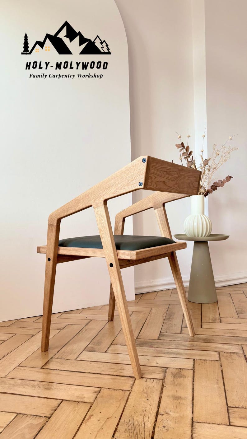 Op de afbeelding: Een moderne houten stoel met een donkergroene zitting en een licht houten frame. De stoel heeft een uniek schuin ontwerp en staat tegen een witte muur. De tekst "HOLY-MOLYWOOD Family Carpentry Workshop" is zichtbaar.