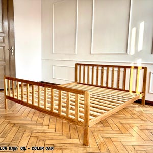 May include: A wooden bed frame with a slatted headboard and footboard, finished in an oak oil stain. The frame features a simple, open design with vertical slats on both ends and a slatted base for mattress support, showcasing the natural wood grain.