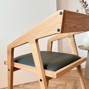 Op de afbeelding: Houten stoel met een donkergroene zitting. De stoel heeft een modern design met een licht houten frame en zwarte hardware. Onderdeel van de Holy-Molywood Family Carpentry Workshop collectie.