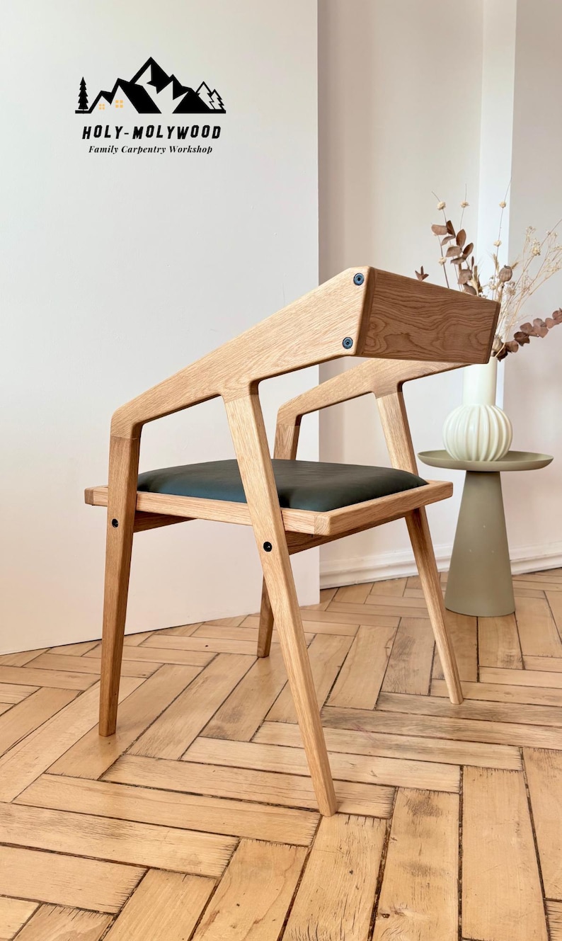 Op de afbeelding: Houten stoel met een donkergroene zitting en een unieke schuine rugleuning. De stoel is gemaakt van lichtgekleurd hout en heeft een modern design. De tekst "HOLY-MOLYWOOD Family Carpentry Workshop" is zichtbaar.