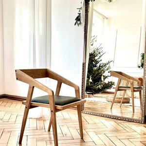 Op de afbeelding: Een houten stoel met een donkergroene zitting en schuine armleuningen. De stoel staat voor een grote spiegel, die de stoel en een kerstboom weerspiegelt. De tekst "HOLY-MOLYWOOD Family Carpentry Workshop" is zichtbaar.