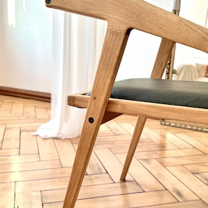 Op de afbeelding: Houten stoel in lichtbruin met een donkergrijze zitting. De stoel heeft een minimalistisch ontwerp met schuine poten en een ondersteunende rugleuning. De stoel is gemaakt van hout en heeft een moderne uitstraling.