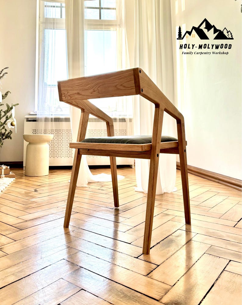 Op de afbeelding: Houten stoel met een minimalistisch ontwerp. De stoel heeft een lichtbruin houten frame en een donkergroen zitkussen. De rugleuning en armleuningen zijn in &eacute;&eacute;n stuk ge&iuml;ntegreerd. De stoel staat op een houten vloer.