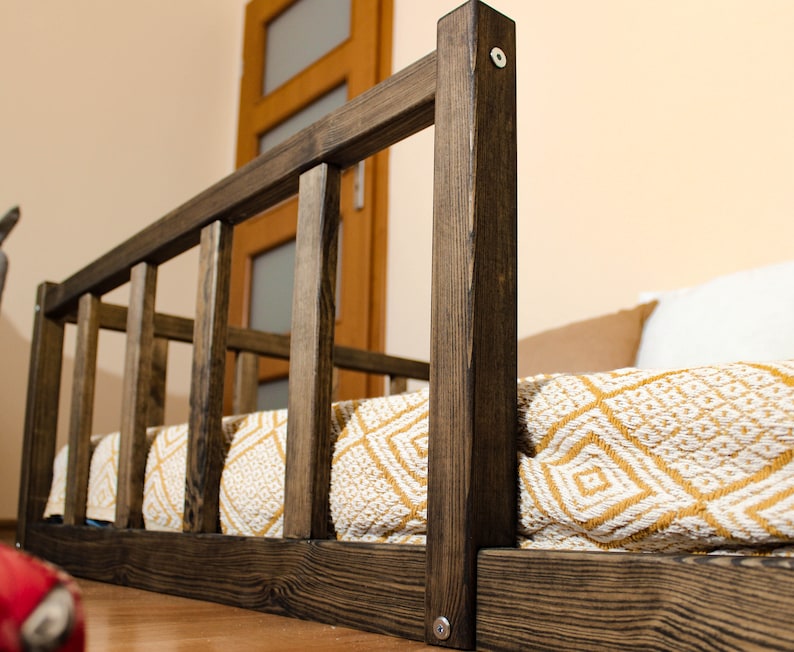 May include: A dark brown wooden dog bed with a white and yellow patterned blanket. The bed has a raised wooden frame with vertical slats.