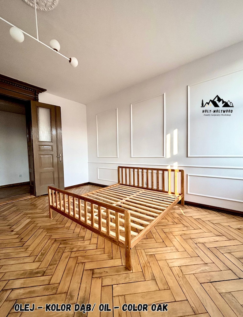 May include: A light brown wooden bed frame with a slatted headboard and footboard, featuring a natural oak oil finish. The frame is constructed with vertical wooden slats and sits on a herringbone patterned wooden floor in a room with white walls.