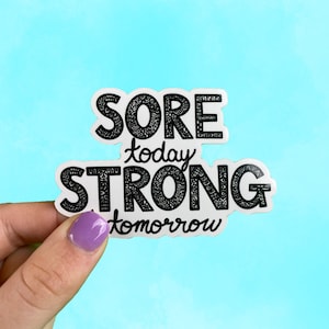 Puede incluir: Pegatina blanca con texto negro que dice "Sore today, Strong tomorrow". El texto está estilizado con un patrón decorativo.