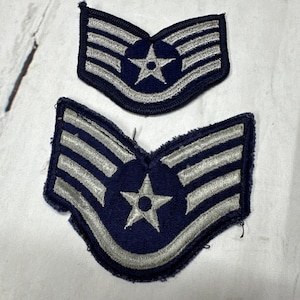 May include: Two vintage Air Force patches. The patches are dark blue with silver stripes and a central star emblem. The patches are embroidered and have a worn appearance, suggesting they are from an earlier era.