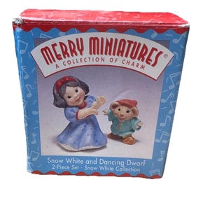 Könnte beinhalten: Eine Schachtel mit einem 2-teiligen Set Schneewittchen und tanzender Zwerg aus der Schneewittchen-Kollektion. Die Schachtel ist blau mit Noten und den Worten "MERRY MINIATURES A COLLECTION OF CHARM". Die Figuren tragen ein blau-weißes Kleid und ein grünes Outfit.
