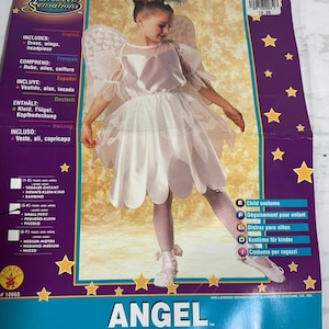 Könnte beinhalten: Weißes Engelskostüm für Kinder, bestehend aus Kleid, Flügeln und Kopfschmuck. Die Verpackung zeigt das Wort "ANGEL" und Größenangaben. Das Kostüm ist für Halloween gedacht.