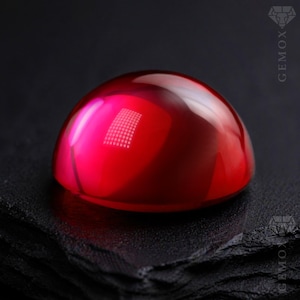 May include: A polished, cabochon-cut gemstone with a vibrant, deep red hue. The smooth, rounded surface reflects light, creating highlights and shadows. The gemstone sits on a textured black surface. The Gemox logo is visible.