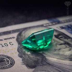 K&ouml;nnte beinhalten: Ein facettierter, smaragdgr&uuml;ner Edelstein liegt auf einem einhundert US-Dollar-Schein. Der Edelstein ist mit mehreren Facetten geschliffen, die das Licht reflektieren. Der Schein zeigt ein Portr&auml;t von Benjamin Franklin.