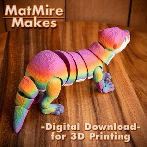 Pode incluir: Uma figura de lontra articulada impressa em 3D com cores de arco-&iacute;ris. A lontra est&aacute; em posi&ccedil;&atilde;o de p&eacute; com a cabe&ccedil;a virada para o lado. O texto "MatMire Makes - Digital Download - for 3D Printing" est&aacute; impresso abaixo da lontra.