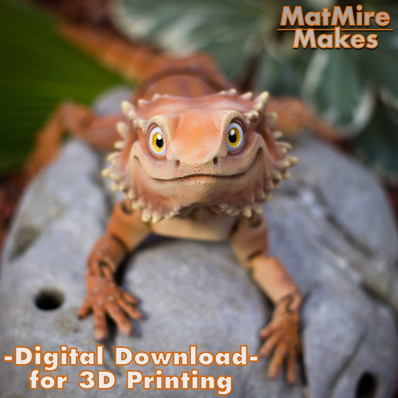 May include: A 3D printed model of a smiling bearded dragon lizard, with orange and brown scales, sitting on a gray rock. The text "MatMire Makes - Digital Download - for 3D Printing" is at the top of the image.