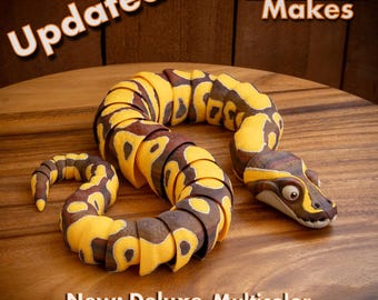 May include: A segmented, articulated snake toy featuring a yellow and brown patterned design. The text "Updated... MatMire Makes" appears at the top, and "New: Deluxe Multicolor .3MF Now Included!" is printed at the bottom of the image.