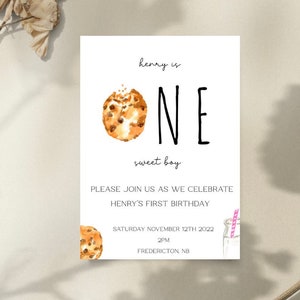 May include: A white invitation card with a watercolor illustration of a chocolate chip cookie. The text on the card reads "henry is one sweet boy" and includes details for a first birthday party.