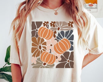 May include: A beige t-shirt with a graphic print of orange pumpkins and brown, blue, and pink flowers.