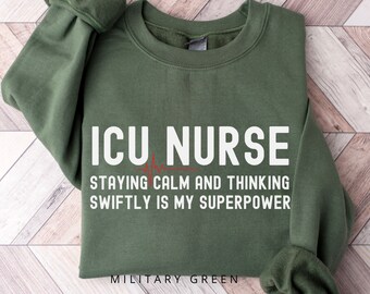 May include: A military green sweatshirt with the text "ICU Nurse Staying Calm and Thinking Swiftly is My Superpower" in white. The text is accompanied by a red heartbeat graphic. The sweatshirt is labeled "Military Green" in red text.