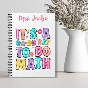May include: A white spiral notebook with the text "Mrs. Jackie" at the top and the phrase "It's a good day to do math" in colorful, playful letters with flowers and stars.