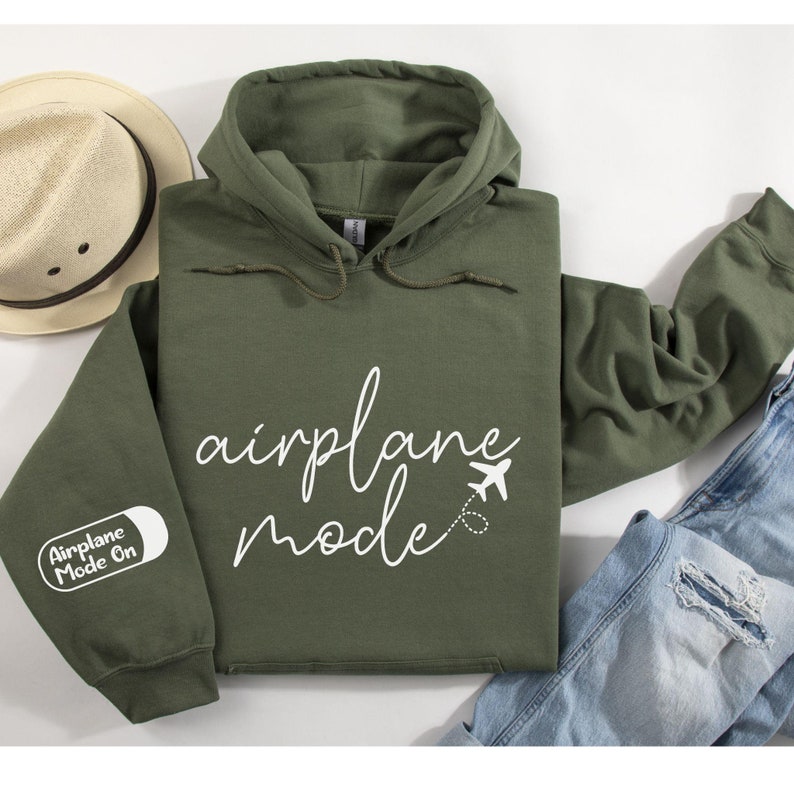 Peut inclure: Un sweat-shirt &agrave; capuche vert avec le texte "airplane mode" en &eacute;criture cursive blanche. Une petite ic&ocirc;ne d'avion est &agrave; c&ocirc;t&eacute; du texte. La manche gauche a un patch blanc avec le texte "Airplane Mode On".