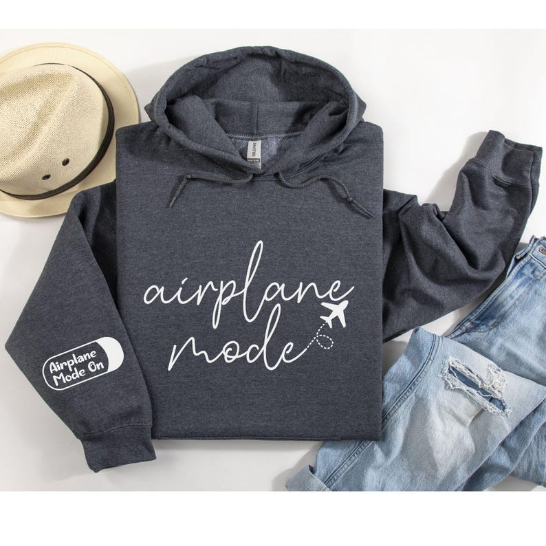 Peut inclure: Un sweat &agrave; capuche gris fonc&eacute; avec le texte "airplane mode" en lettres cursives blanches. Une petite ic&ocirc;ne d'avion est &agrave; c&ocirc;t&eacute; du texte. La manche gauche a un patch blanc avec le texte "Airplane Mode On".