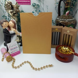 May include: A gold envelope with a flap on the top, a pink wax seal with a tree design, a string of gold beads, and two boxes of wax sticks. The boxes are labeled "Davetiye Dunyasi" which translates to "Invitation World".