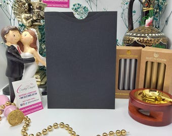 Può includere: Una busta nera per biglietti da visita con una fessura ritagliata per un biglietto. La busta è su un tavolo con una catena dorata, un porta timbri in legno e due scatole di sigilli di cera. Le scatole di sigilli di cera sono etichettate con "Davetiye Dunyasi" in lettere dorate.