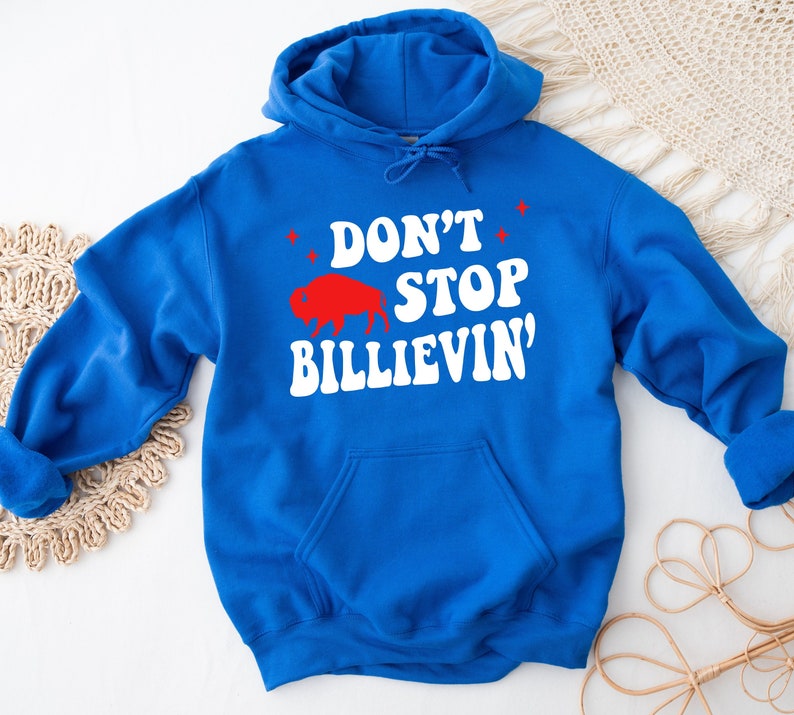 Puede incluir: Una sudadera con capucha azul real con un gr&aacute;fico blanco que dice "Don't Stop Billievin'" con una silueta de b&uacute;falo roja.