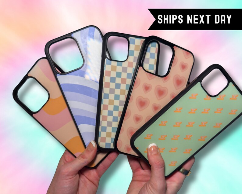 May include: Five different phone cases with various patterns. The cases are black with a clear plastic back. The patterns include orange and pink waves, blue and white stripes, a checkered pattern, pink hearts, and green with orange symbols.
