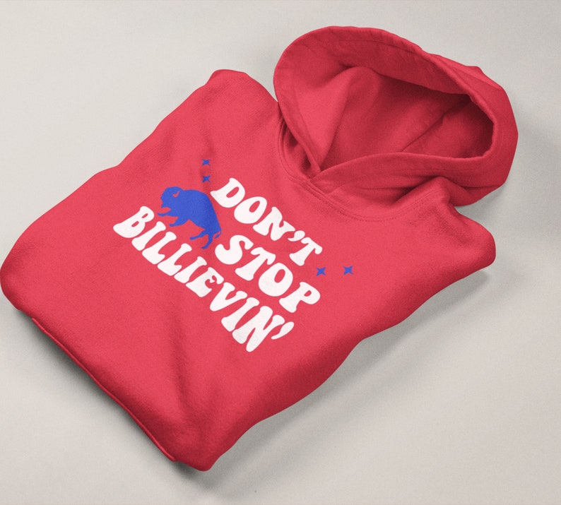 Puede incluir: Sudadera con capucha roja con texto blanco que dice "Don't Stop Believin'" y una silueta de b&uacute;falo azul.