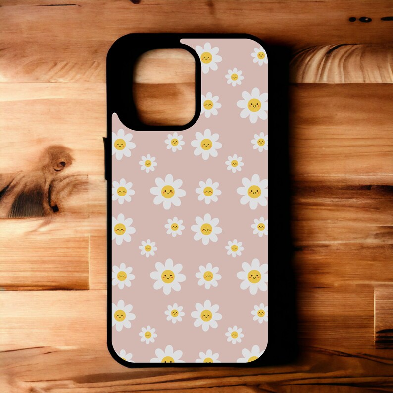 May include: A black phone case with a pink background and a pattern of white daisies with yellow centers and smiling faces.