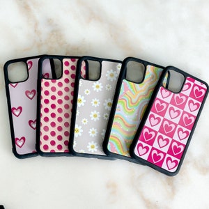 May include: Five different phone cases with various patterns. The cases are black with pink and white designs. The designs include hearts, polka dots, flowers, and wavy lines.