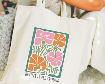 May include: A white canvas tote bag with a floral design in shades of pink, orange, and green. The text "BEAUTY IS ALL AROUND" is printed on the bag.