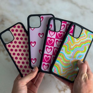 May include: Four different phone cases with various patterns. The cases are black with pink, white, and blue designs. One case has a polka dot pattern, another has a checkered pattern with hearts, another has a swirl pattern, and the last one has a heart pattern.