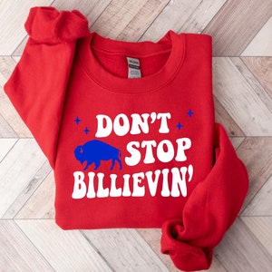 Puede incluir: Sudadera roja con una silueta de b&uacute;falo blanca y el texto "Don't Stop Billievin'" en blanco.