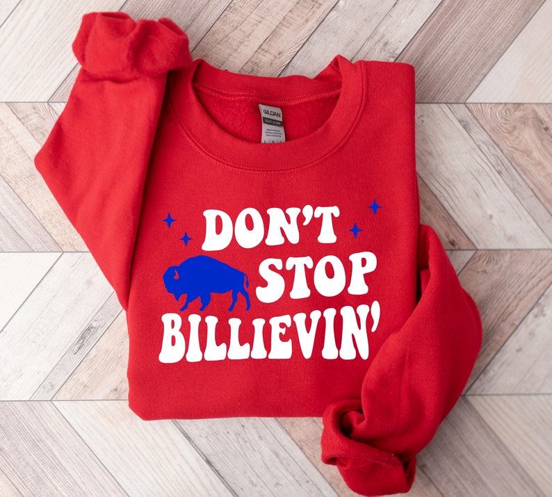 Puede incluir: Sudadera roja con una silueta de b&uacute;falo blanca y el texto "Don't Stop Billievin'" en blanco.