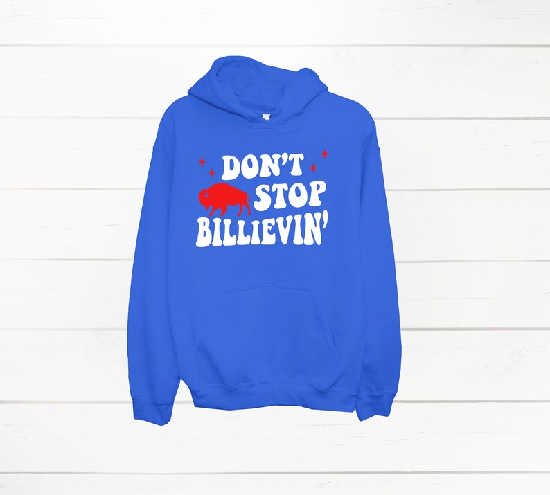 Puede incluir: Una sudadera con capucha azul real con un gr&aacute;fico blanco que dice "Don't Stop Billievin'" con una silueta de b&uacute;falo roja.