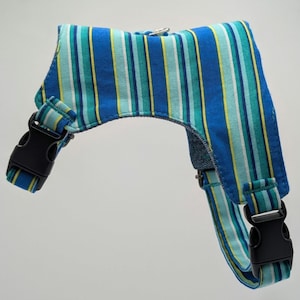 May include: A dog harness with blue and green vertical stripes and black plastic buckles. The harness has a design of blue, green, and yellow stripes. The harness is designed to fit around the dog's chest and back.